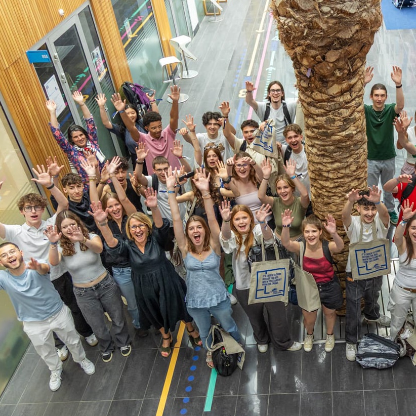 Un grand groupe d'élèves lève les bras dans le hall du lycée