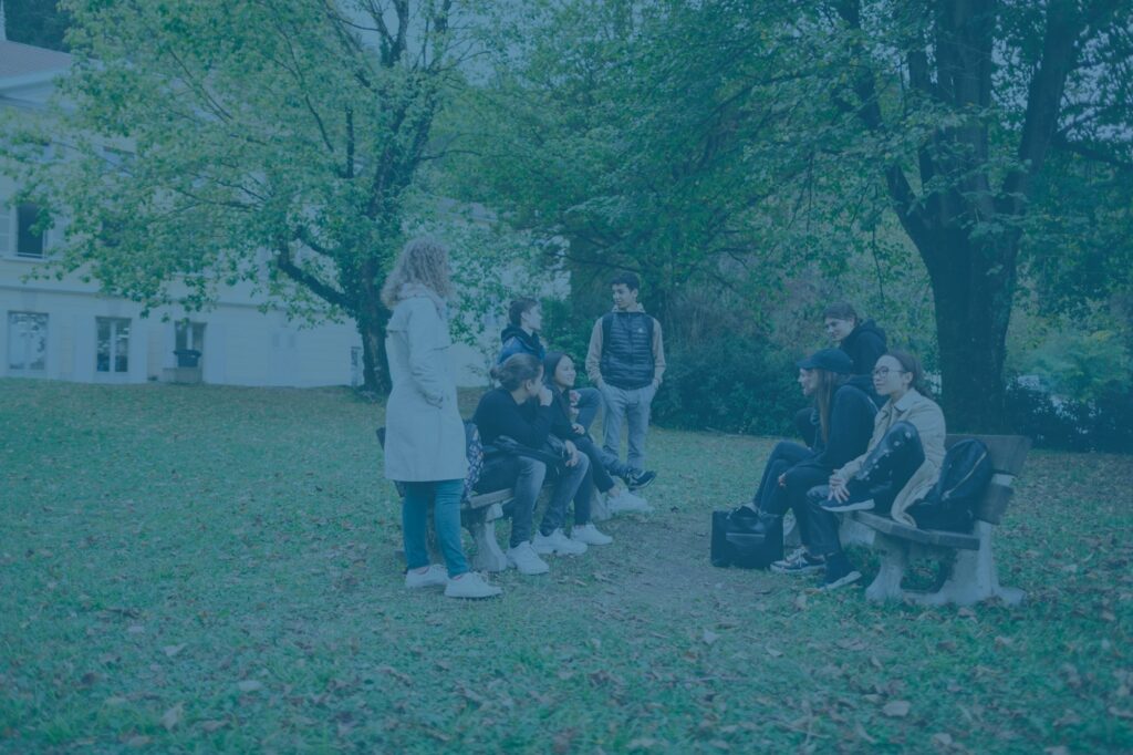 Des élèves assis sur des bancs sous les arbres du parc du lycée