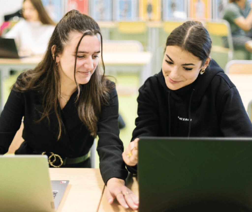 Deux étudiantes souriantes devant un ordinateur portable, à l'extérieur