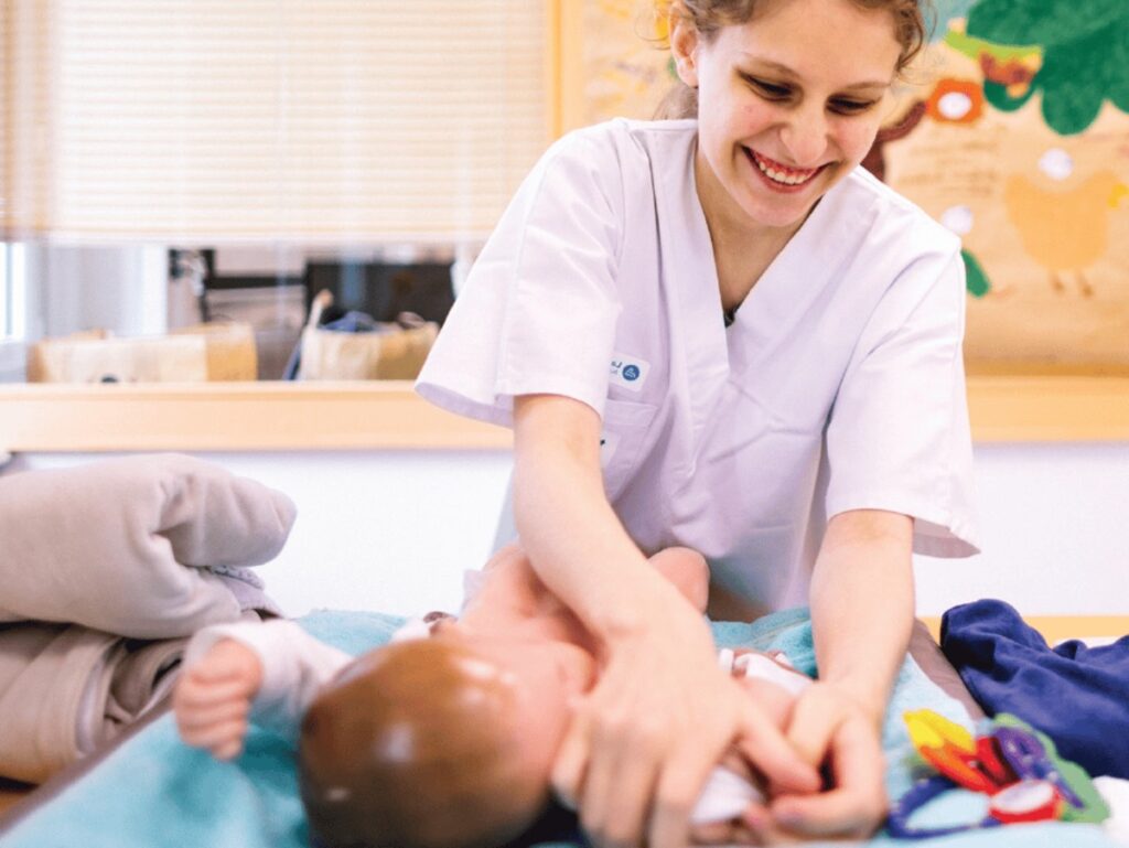 Une élève en blouse blanche s'occupe d'un bébé sur une table de change