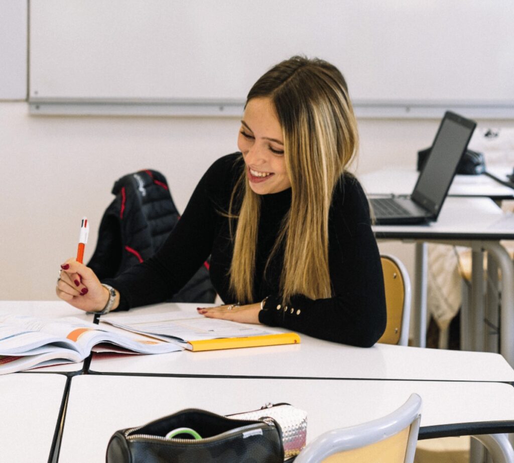 Une élève prend des notes à sa table, entourée de ses livres