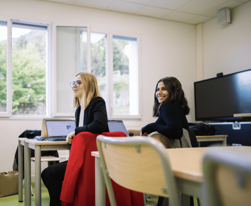 Deux élèves assises sur les tables près de la fenêtre d'une salle de classe