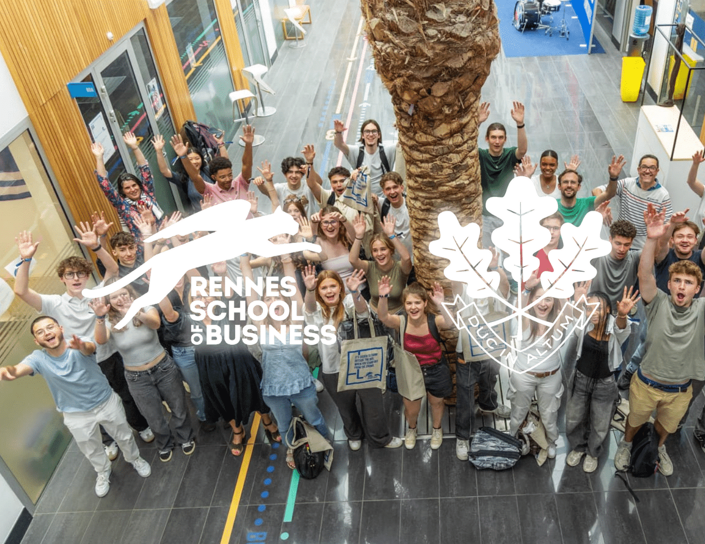 Un grand groupe d'élèves lève les bras dans le hall, logo Rennes School of Business