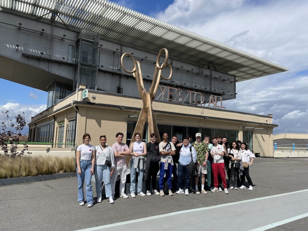 Groupe d'élèves réuni en extérieur devant un bâtiment moderne surmonté d'une sculpture